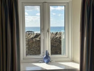Window with a wall and sea view outside. On inside is a blue vase